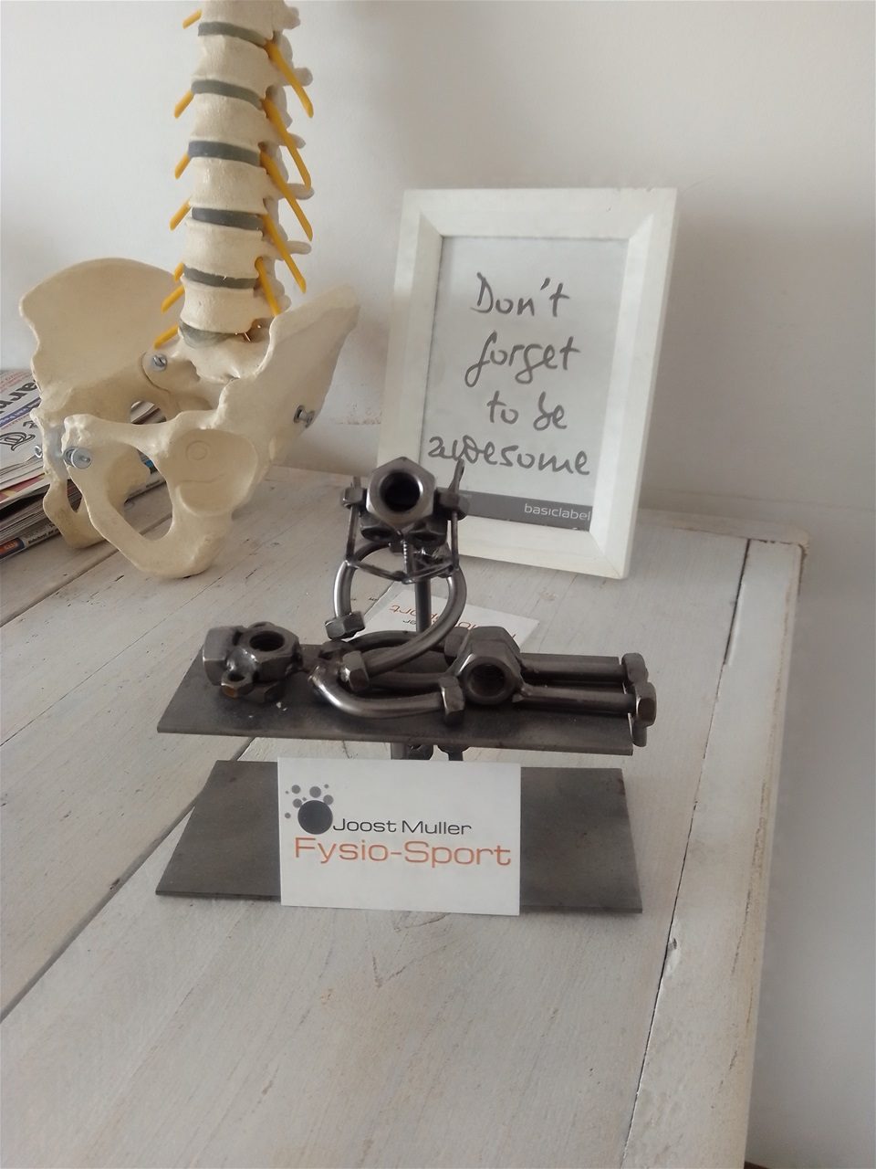 Visitekaartje van Joost Muller Fysio-Sport, met een anatomisch bekkenmodel en een fotolijstje op de achtergrond